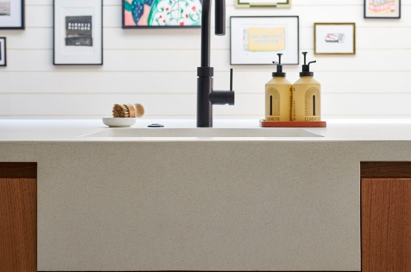 View of a sink area with a concrete bowl built within the work surfaces, with wood base cabinets, and a black boiling-water tap.