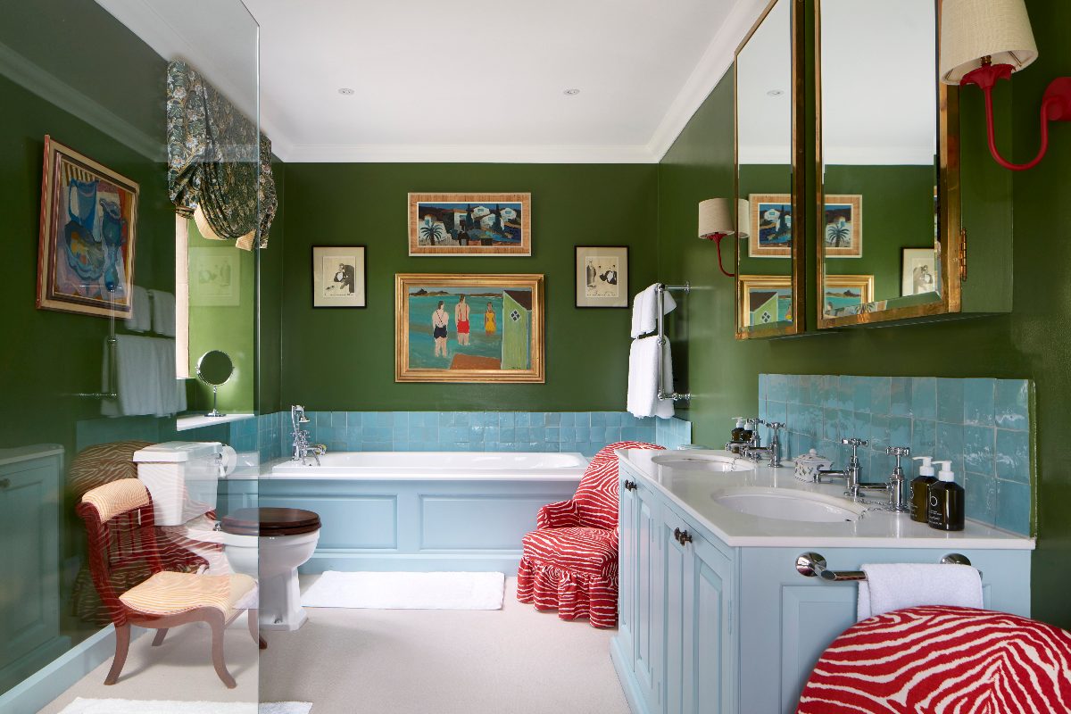 A playful bathroom design with dark green wall paint, a blue fitted tub, and a matching double vanity unit.