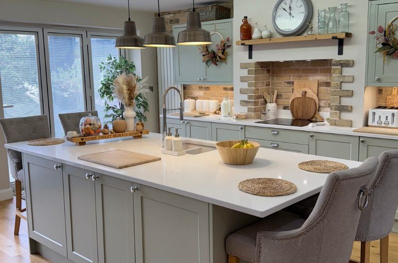 A timeless kitchen design painted in a sage colour with white worktops and wood and brick finishes.