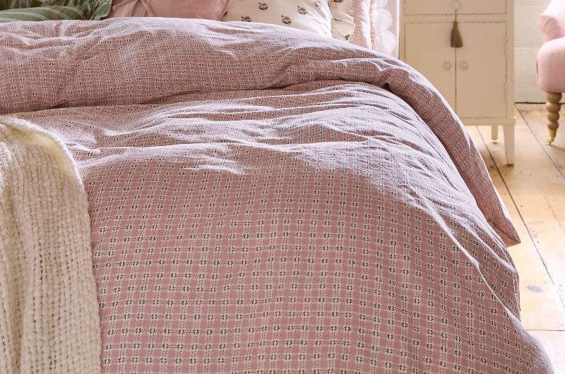 A rustic, romantic sleep space with a blue scalloped headboard, gingham bedding, and off-white furniture and panelling.