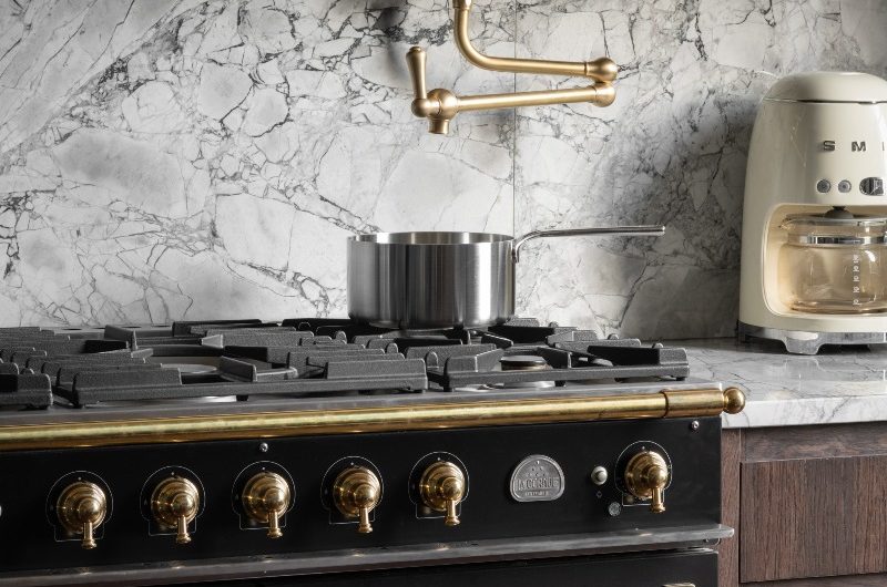 Closeup at a black range cooker with gas hob and brass pot filler tap above it, with statement stone surfaces.