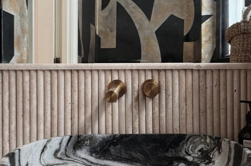 Closeup at a vanity zone with a dark stone basin, fluted wall tiles, and a mirror.