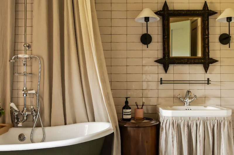 A country chic bathing space with a green painted tub with chunky shower curtains, a traditional basin with a sink skirt and rustic decor.