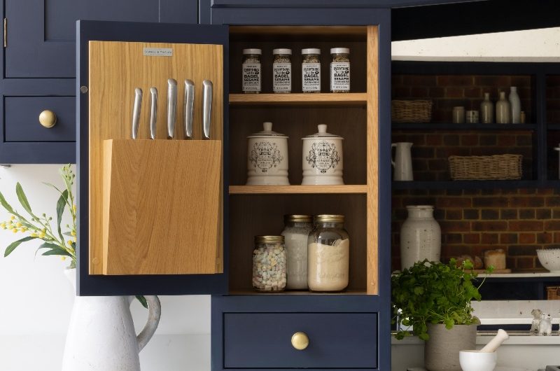 A dark blue kitchen with white surfaces and slim cupboards and drawers on both sides of the cooker which featrue oak internal shelving.