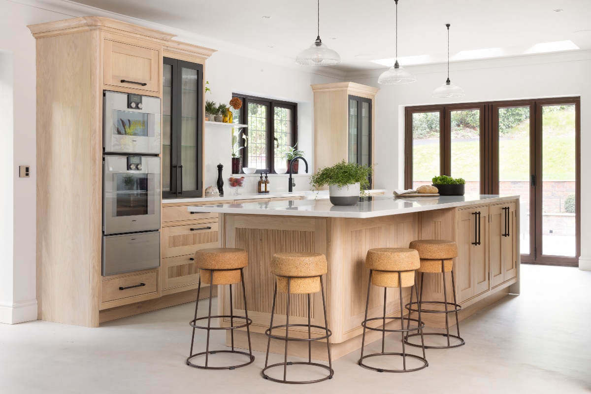 A Scandi kitchen with an island, bar stools, a main cabinetry run with built-in appliances and glass fronted doors.