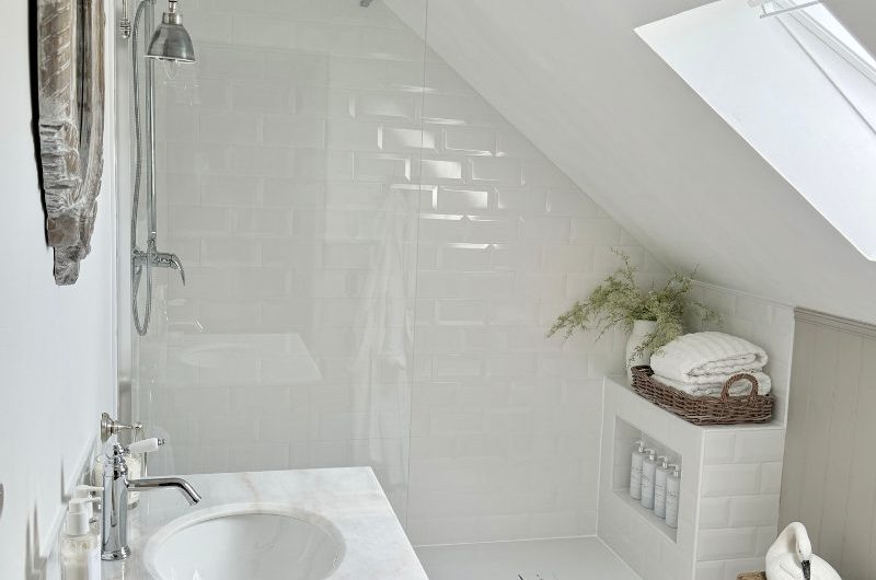 A light and bright bathroom renovation with metro tiles, storage nooks, wood furniture, and patterned floor tiles.