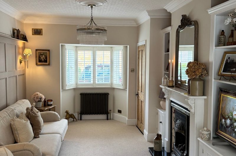 A calm living room with neutral carpet, plush seating, a fireplace, and wooden beams.