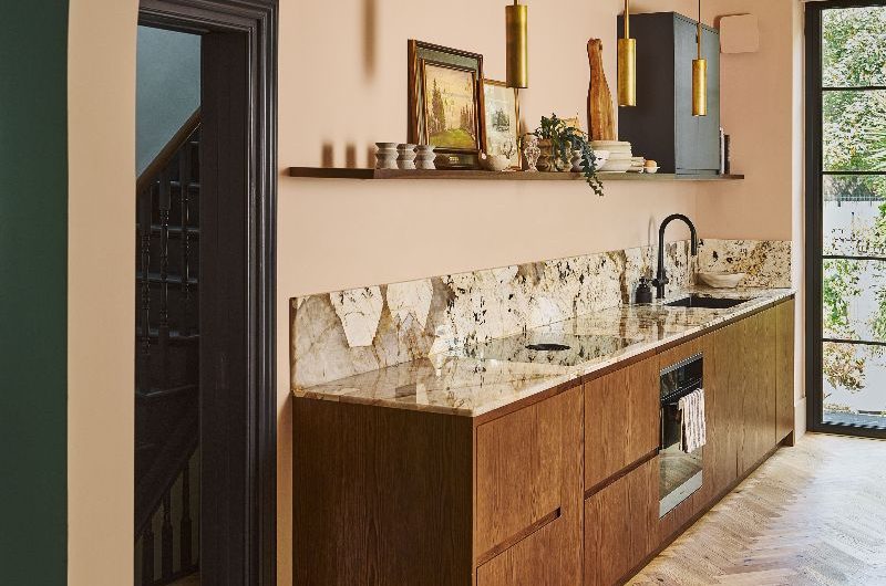 A modern kitchen design layered in wood finishes, with a darker walnut on the cabinetry run and lighter, grainy material on the floor, with stone surfaces and minimalist decor.