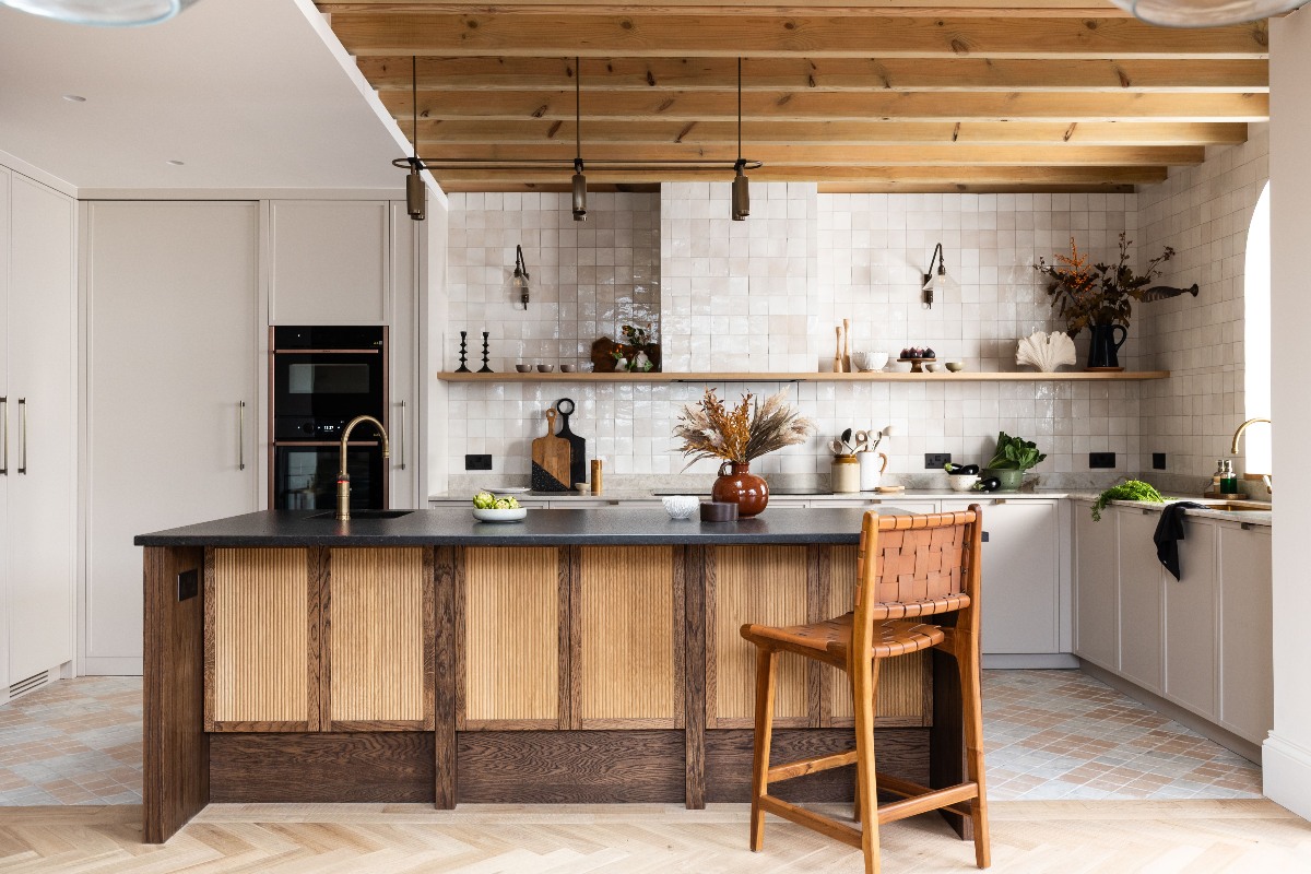 A modern scheme with slim shaker kitchen cabinets, tiled walls and extractor canopy, and a central wood island with a fluted finish and dark work surface.