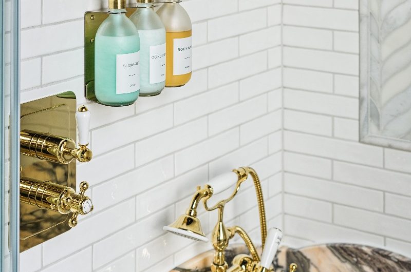 A bath zone with wall-mounted bottle storage, gold brassware, metro tiles, and a pink marble bath surround.