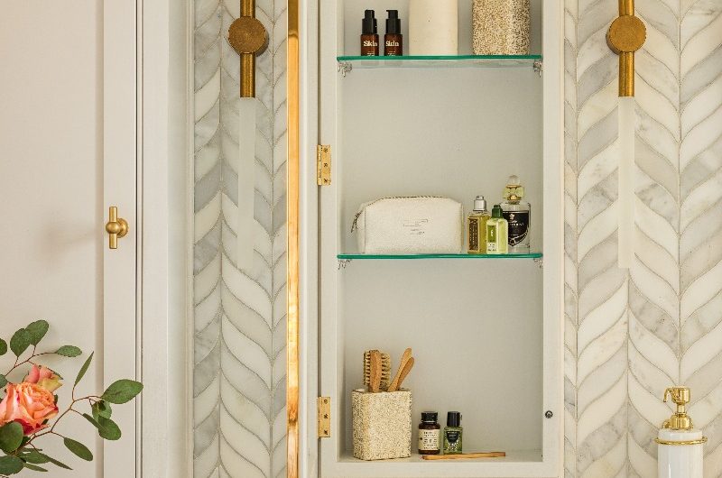 Closeup at the recessed mirror with shelving, marble tiles, and gold accents.