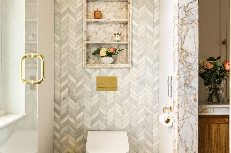 A smart WC, gold fittings, and the back wall cald in marble leaf mosaic tiles, and an alcove for storage above it.