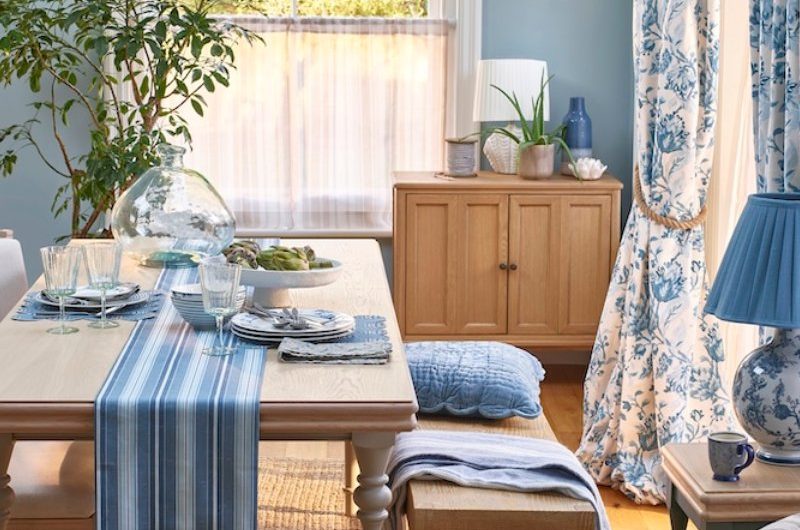 A coastal dining room with blue walls, a wood table and bench, and a striped armchair.