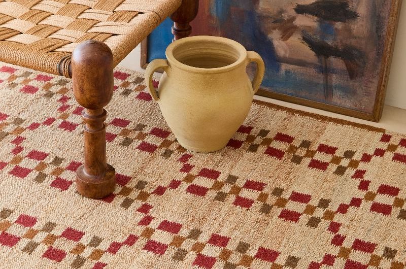 A flatweave jute rug with a handcrafted stool, yellow vase, and art.
