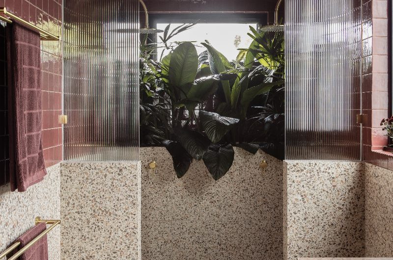 A spa-like bathroom with terrazzo tiles, burgundy zellige, fluted panels, gold hardware, and house plants.