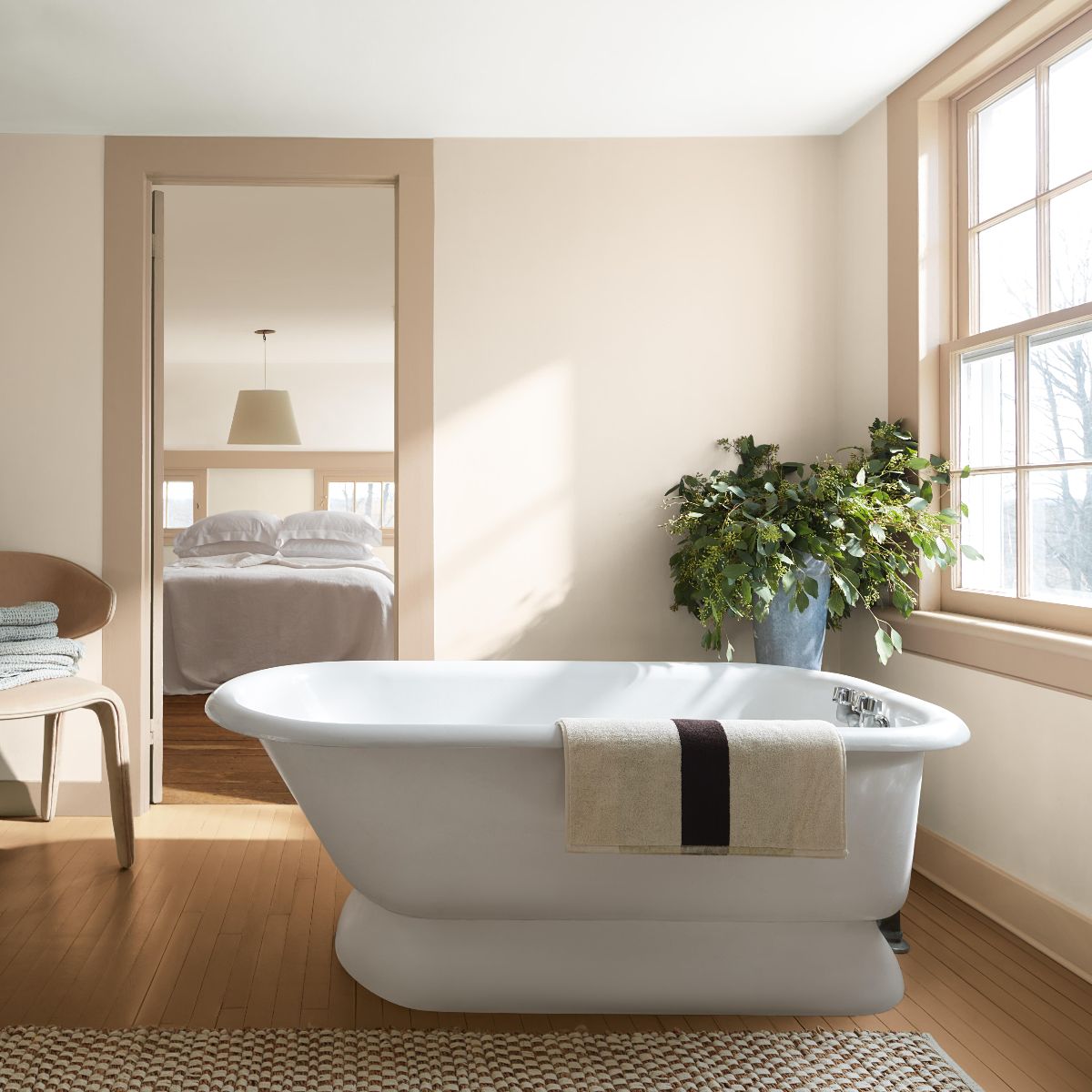 A calm ensuite with neutral wall paint, a freestanding tub, wood flooring, and house plants.