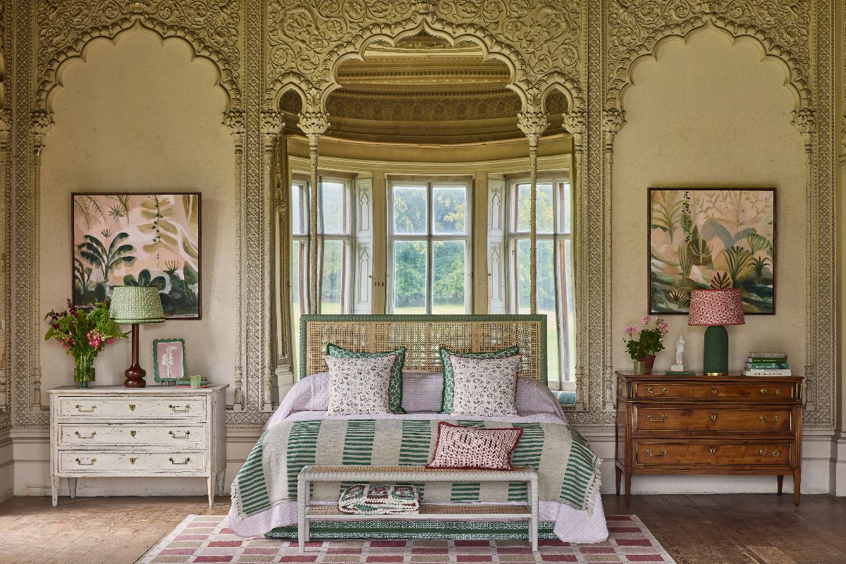 A globally inspired bedroom with a rattan bed, patterned linen, antique side boards, and exotic wall art.