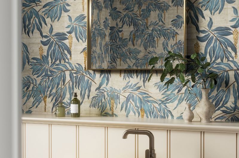A cloakroom with timeless neutral panelling and blue patterned wallpaper, a butter yellow basin, and brass accessories.