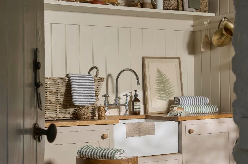 A utility with wall panelling, neutral cabinetry, wooden worktop, with a butler sink and chrome tap, and decor made from natural materials.