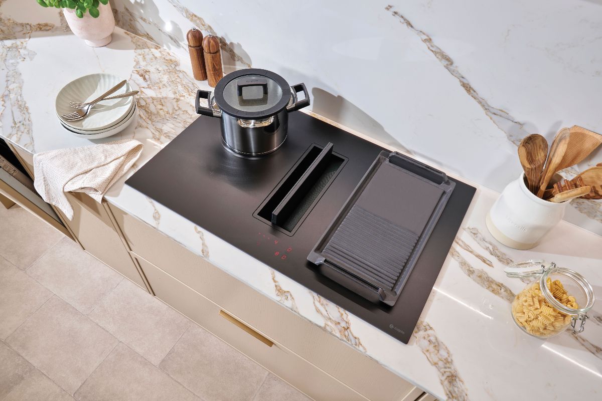 A modern kitchen design with an extractor hob with a matt finish, sleek neutral cabinets, and veiny surfaces.