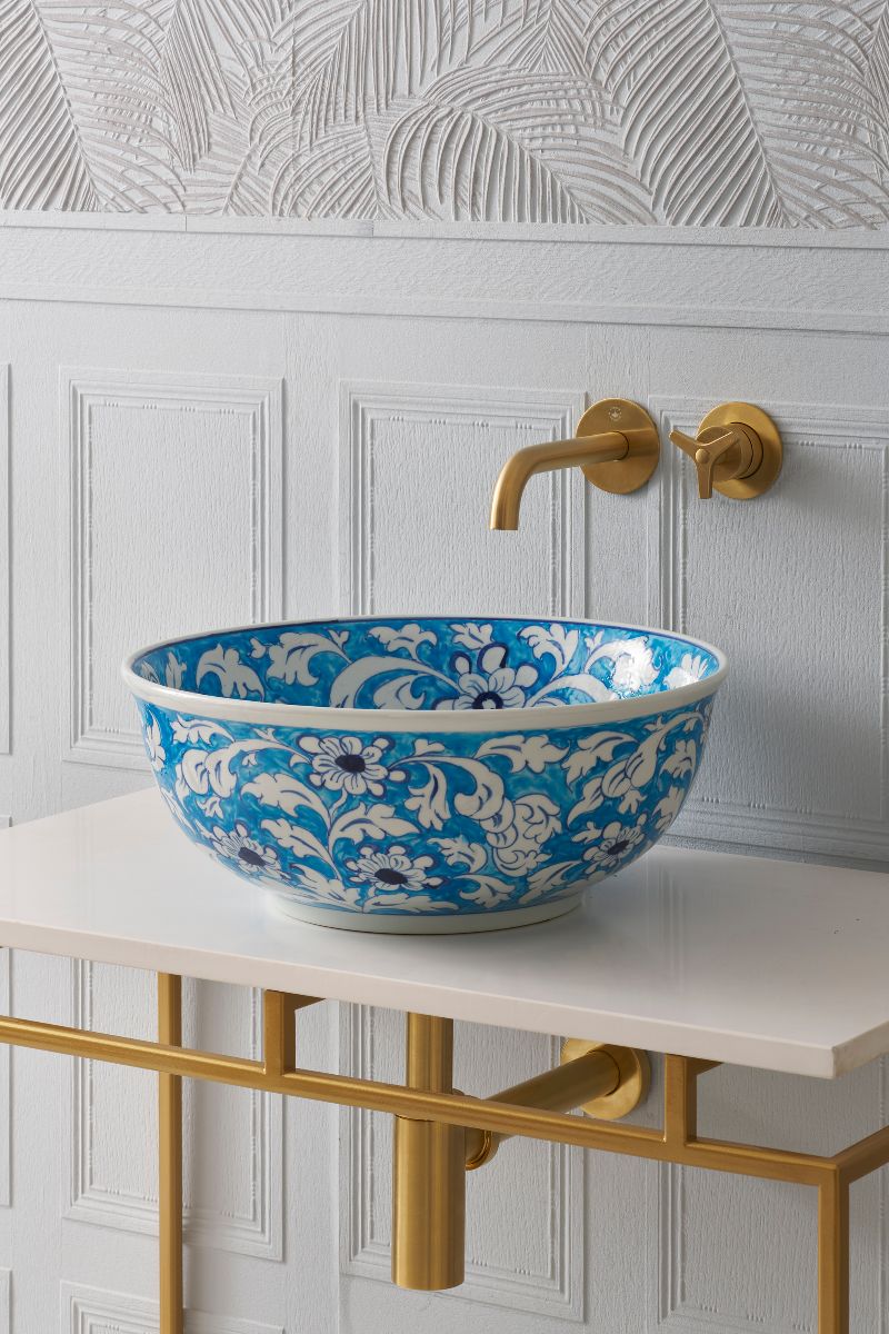 Closeup at a blue basin with white flowers and leaves on a simple vanity with a gold frame.