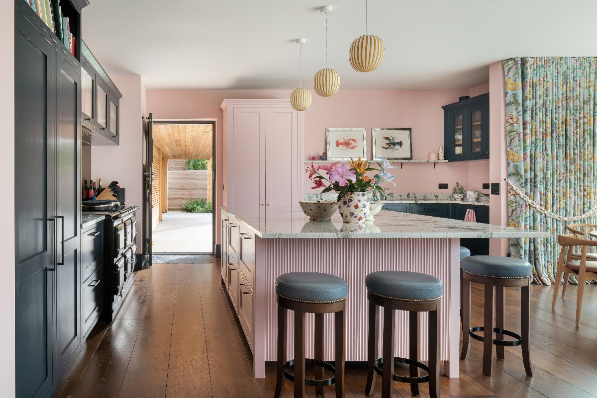 A colourful kitchen with a pink fluted island and dark wood flooring.