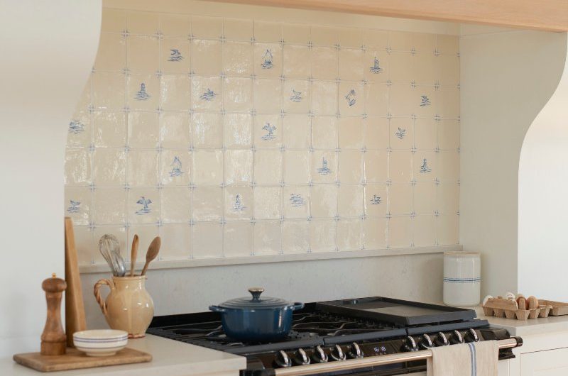 A cooking zone with delft tiles, a white range cooker, white cabinetry, and a wooden mantel.