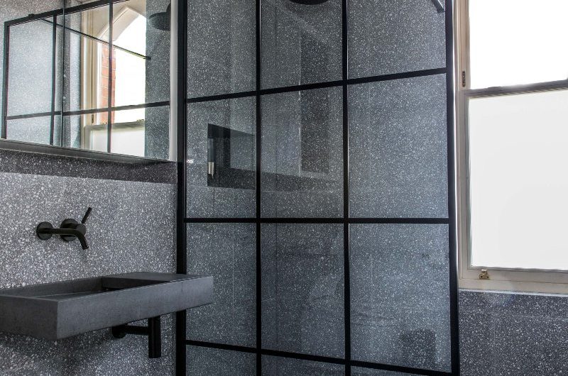 A terrazzo bathroom with speckled tiles, a black-frame enclosure and concrete basin.