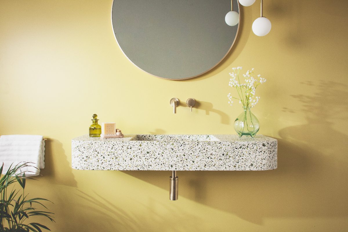 A yellow scheme with a speckled basin, gold tap, and round mirror.
