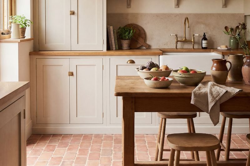 A country kitchen design with terracotta flooring, cream Shaker cabinets and a freestanding bakers table.