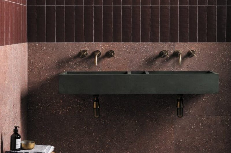 A dark green concrete basin in a burgundy bathroom with long metro wall tiles on the upper half of the wall and terrazzo on the bottom half and floor.