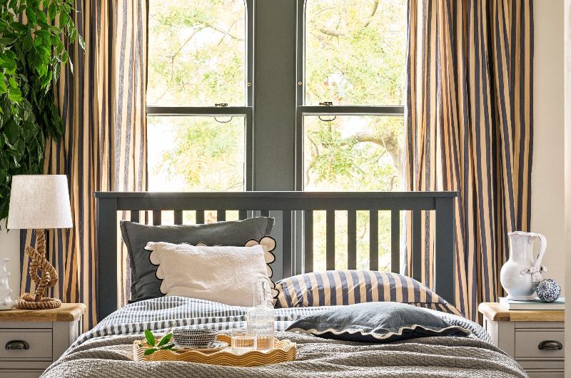 A coastal bedroom with a bed centred in front of the window, with striped soft furnishings, classic bedside tables, and a knot lamp.