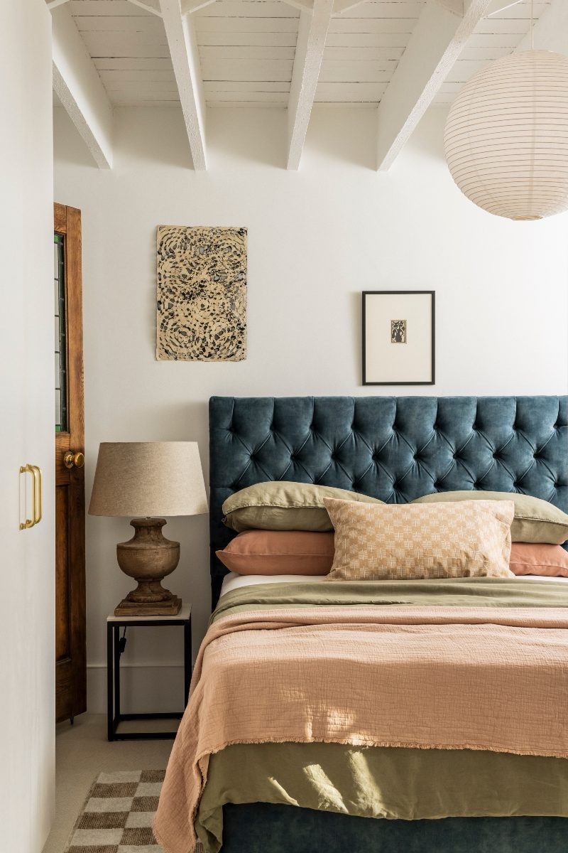 A calm bedroom design with global design inspiration, a blue headboard, and rustic decor.