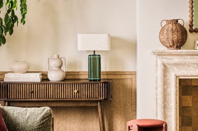 A spring living room with wood panelling, stone fireplace, a fluted wood sideboard, a green sofa, and jute rug.