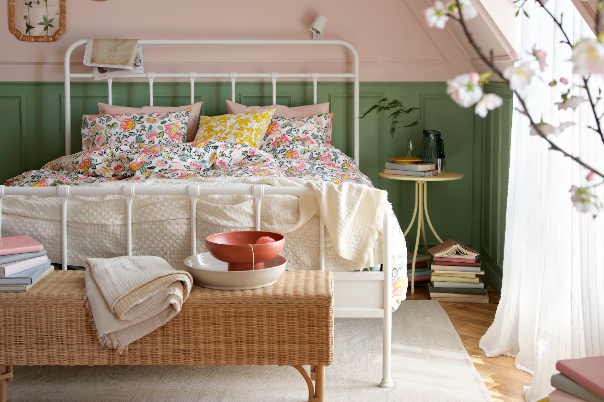 A calm bedroom design with green panelling, blue wall paint, steel white bed frame, a rattan ottoman, and floral bedding.