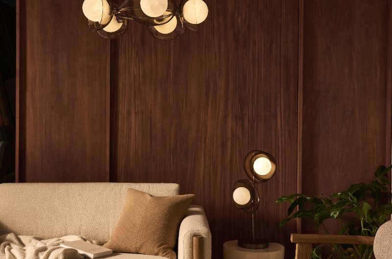 A living room with an new Deco allure with dark wood panelling, neutral seating solutions, and metallic lighting.