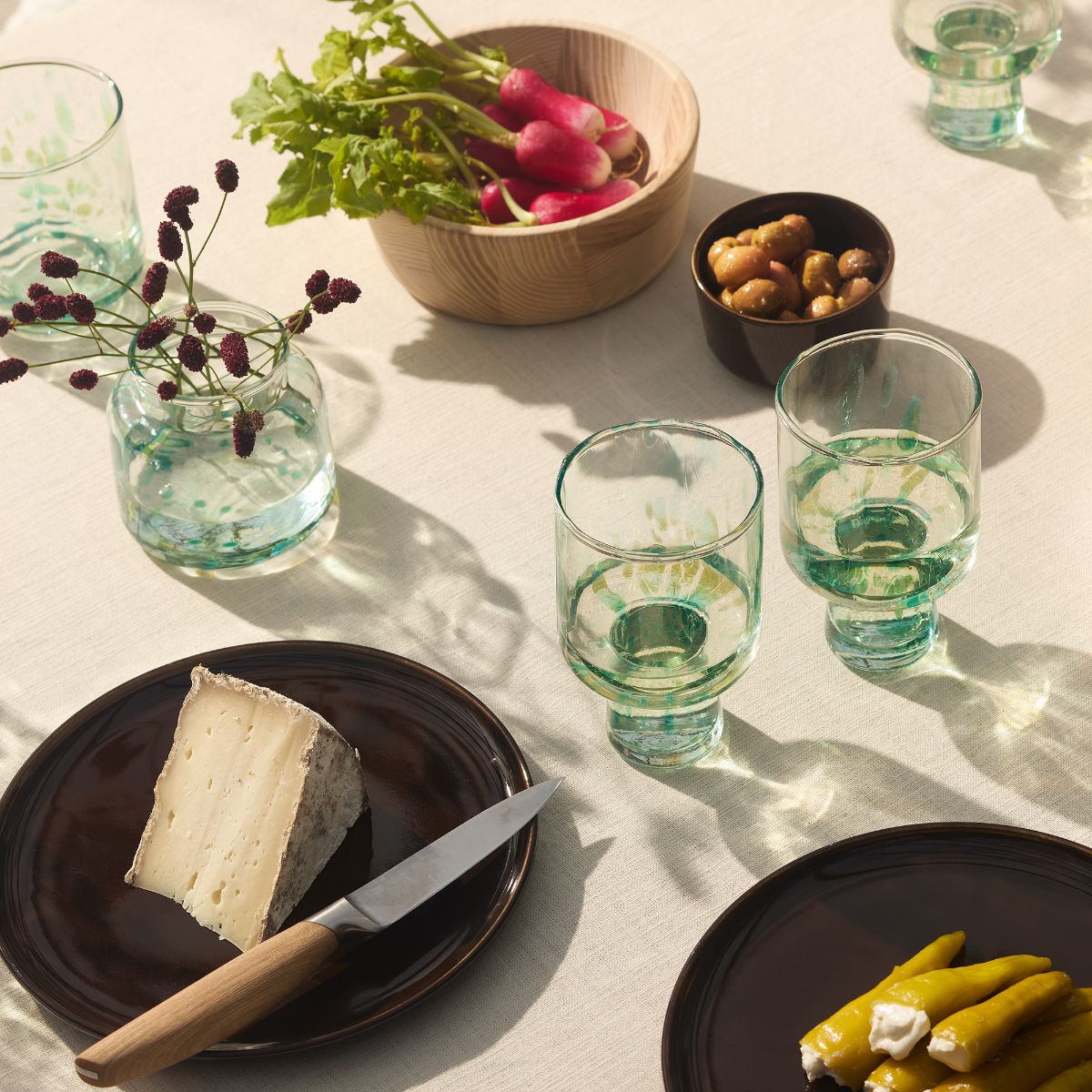 A Mediterranean table with glossy brown plates, green glassware, and wood cutlery.
