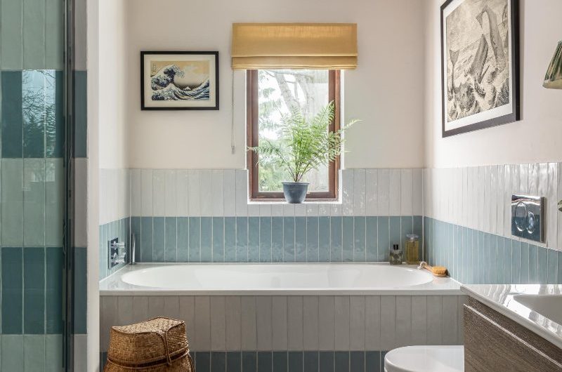 A calm bathroom design with a shower, fitted bath, blue and white tiles, and a wood vanity unit.