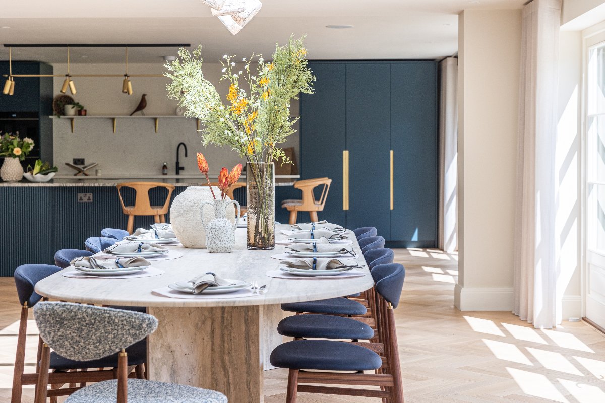 A modern kitchen design with blue cabinetry, a fluted island, and a large dining zone with a marble table and blue chairs.