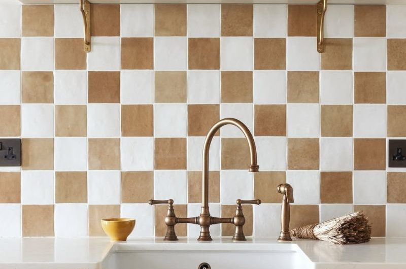 A kitchen design with ochre cabinetry, a butler sink, brass tap, and checkerboard flooring, with open shelving above it.