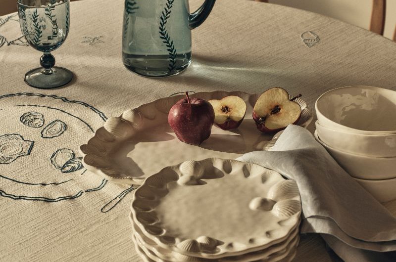 A coastal living room with an embroidered table cloth, blue glassware, and organic tableware.