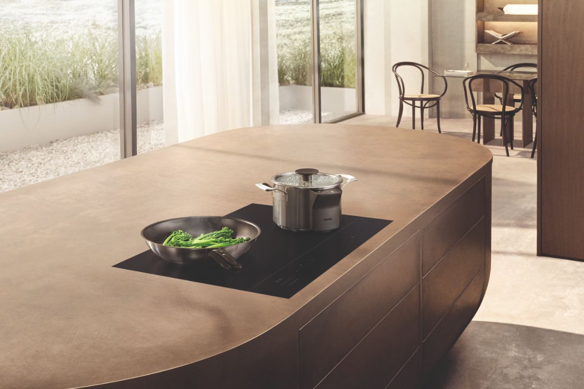 A modern scheme with a tactile island with built-in cooking appliance and storage, a dining zone, and ample glazing.