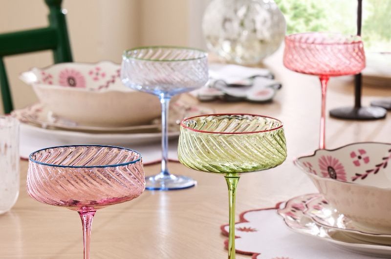 A spring tablescape with coloured glassware and patterned crockery on a wooden table.
