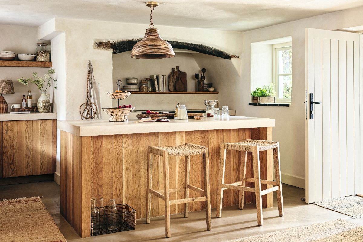 A country kitchen design with a wood island with rattan bar stool, plaster on the walls, rustic decor, and jute rugs.