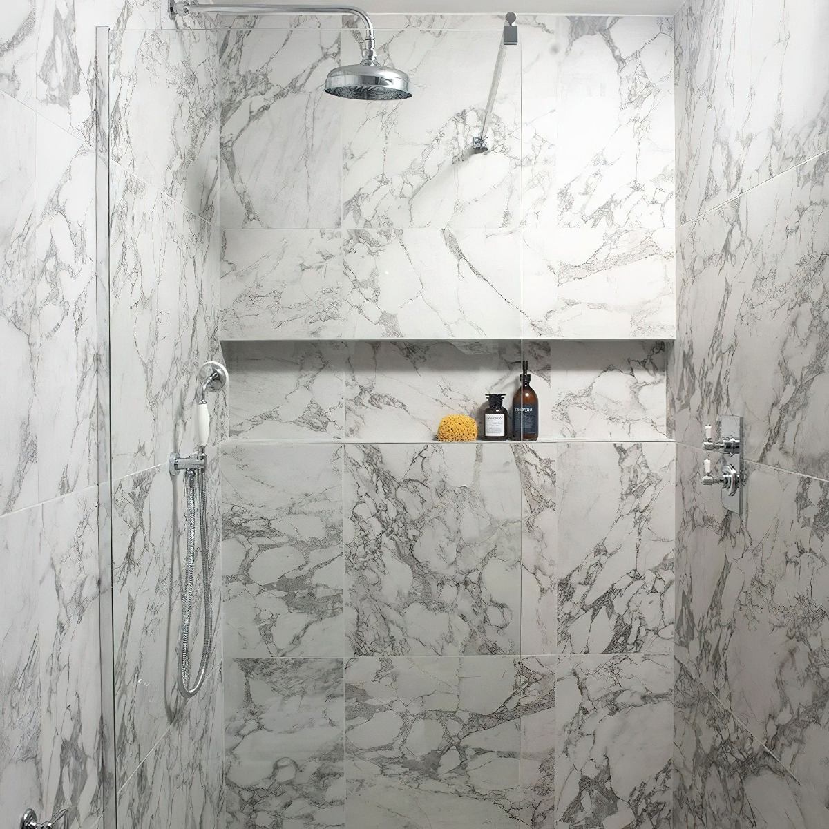 A bright shower design with marble tiles, chrome brassware, and a storage niche.