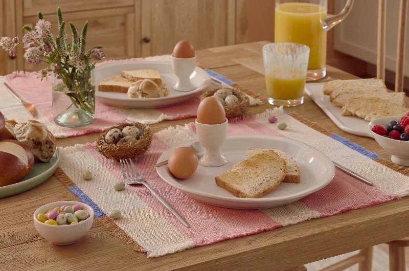 A rustic dining table made from wood, with pastel decor and white ceramics.