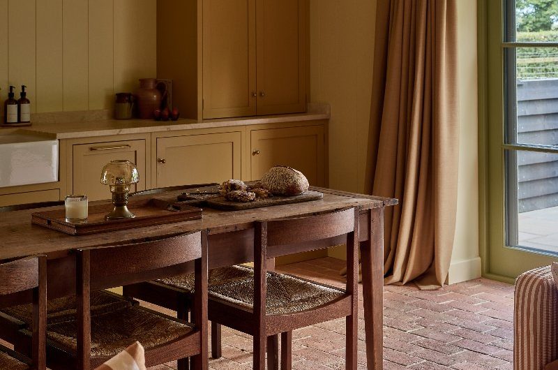 Yellow Mediterranean style kitchen with rustic floor tiles, a dark wood dining table and chairs, and wall panelling.