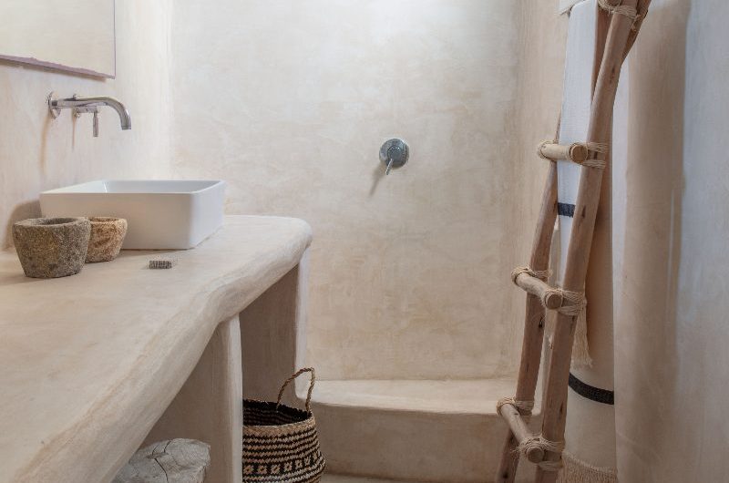 A spa-like bathroom with wood-effect flooring, plastered walls and vanity, and wood decor.