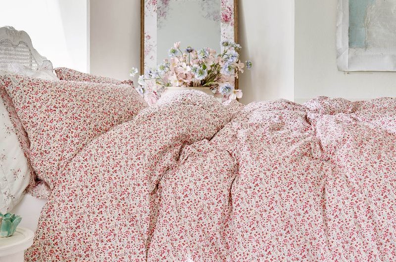 A romantic bedroom for spring and summer with floral bed linen, wood flooring, and airy curtains.