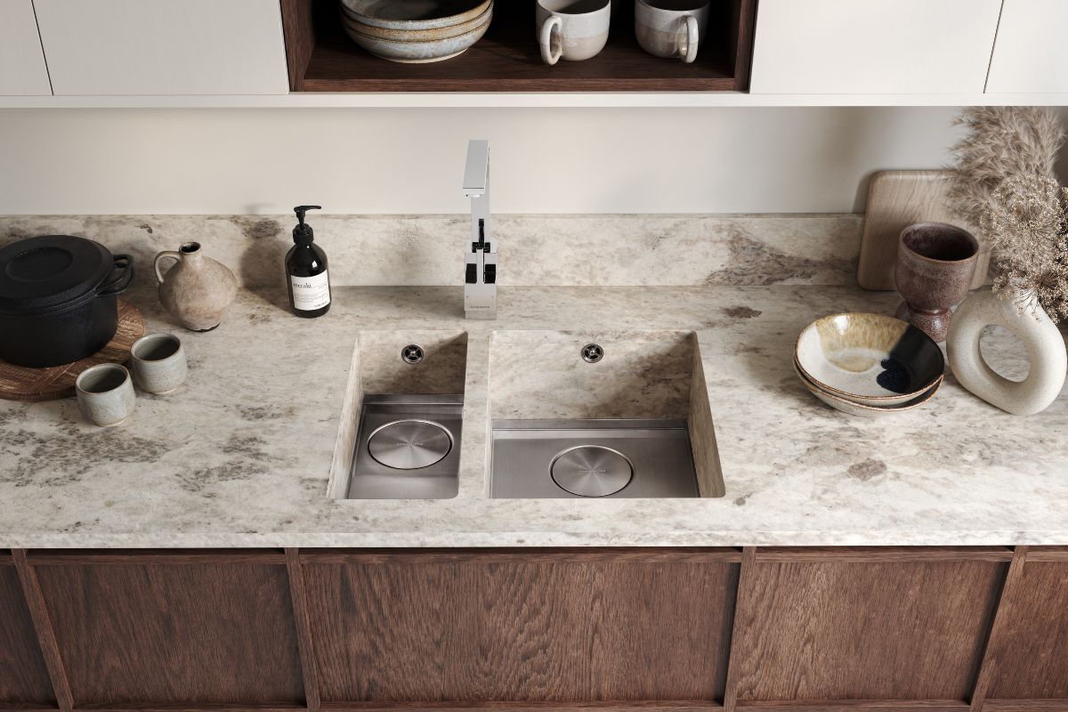 Closeup at a sink zone with marble worktops, wood cabinets and organic decor.